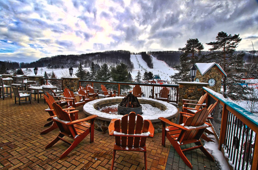 an image of a fire pit with 12 red Adirondack chairs around it and the ski slope in the background